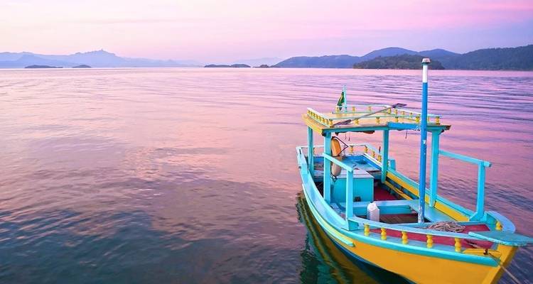 Buntes Holzboot, das bei Sonnenuntergang auf ruhigen rosa und violetten Gewässern treibt