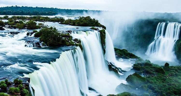 Las poderosas cascadas de las Cataratas del Iguazú se despeñan en un desfiladero lleno de niebla rodeado de exuberante bosque verde.