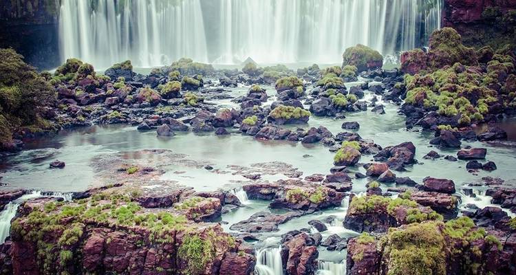 Cortinas de agua en varios niveles se desploman sobre rocas cubiertas de musgo en la base de las Cataratas del Iguazú.