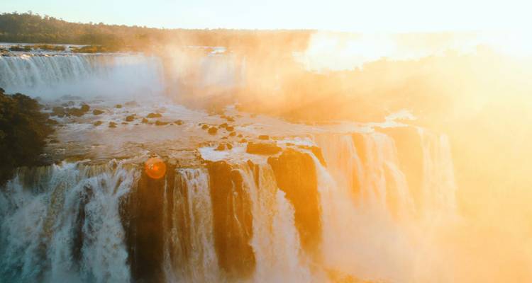 La lumière dorée du soleil et les embruns créent une lueur dramatique au-dessus des imposantes chutes d'Iguazu.