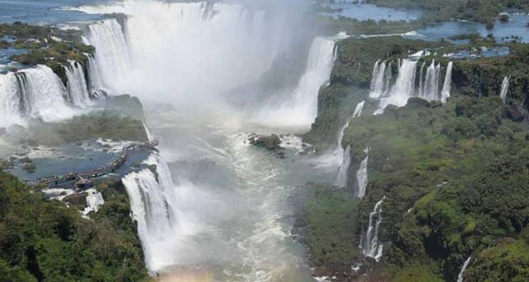 Luchtfoto van de enorme Iguazu-watervallen die in een mistgevulde kloof storten, omgeven door groen.