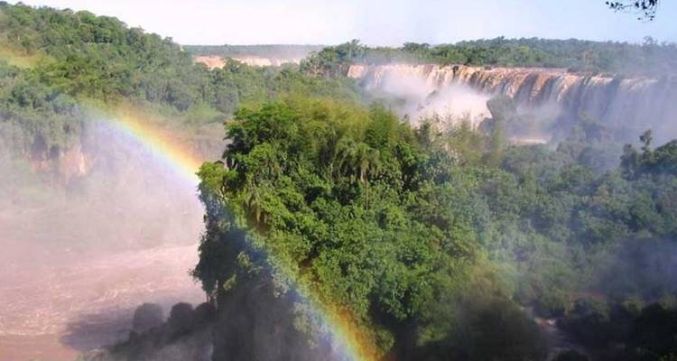 Een felle regenboog spant zich uit boven mistige jungle en de cascade van de Iguazu watervallen.