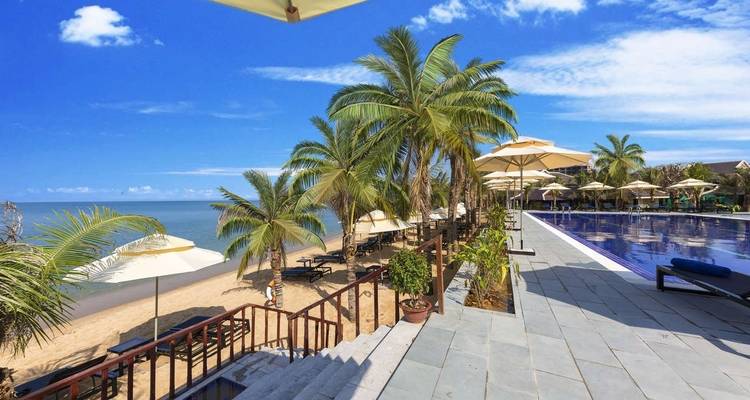 Een resortbad naast een strand onder een heldere hemel, omzoomd met palmbomen.