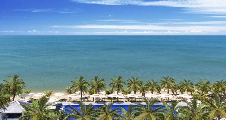 A pool with lounge chairs overlooking the ocean on a clear day.