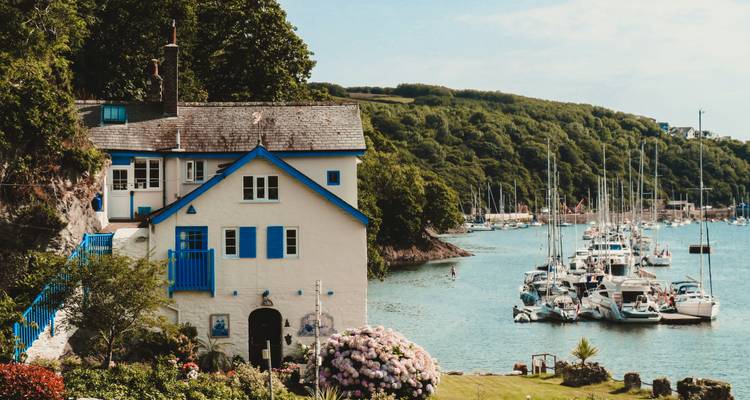 Una encantadora casita blanca y azul que tiene vistas a una marina llena de veleros y colinas verdes.