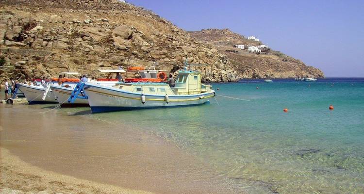 Barcos en una playa arenosa con aguas azules cristalinas y fondo rocoso.