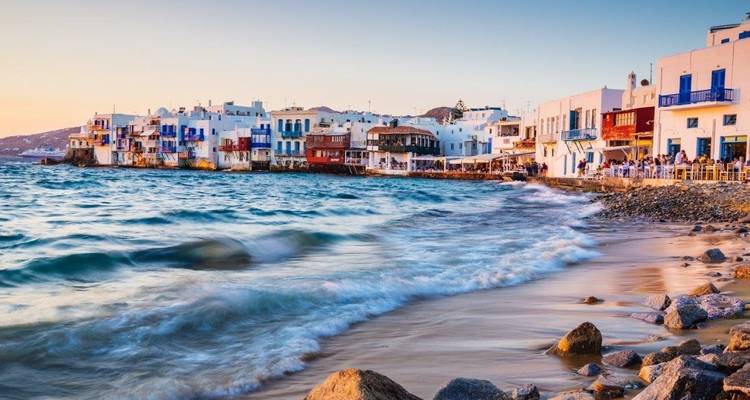 Ville côtière à Mykonos au coucher du soleil avec des vagues frappant le rivage.