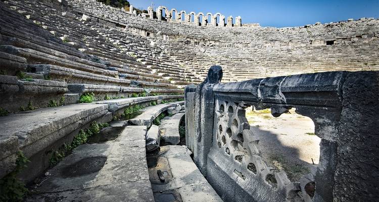 Ruinas de un teatro antiguo con asientos de piedra y tallados decorativos.