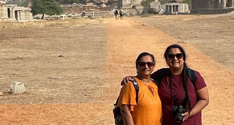 Two women smiling and posing on a path with ancient ruins in the background.