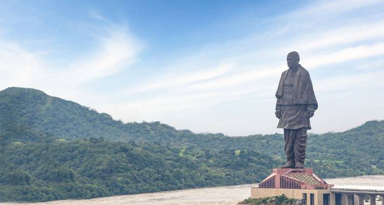 Grande statue dans un paysage pittoresque avec des collines vertes et une rivière.