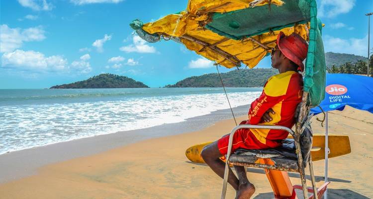 Un sauveteur en uniforme surveillant une plage ensoleillée avec des parasols.