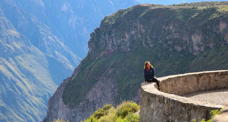 Une personne assise sur un mur de pierre surplombant un vaste paysage montagneux.