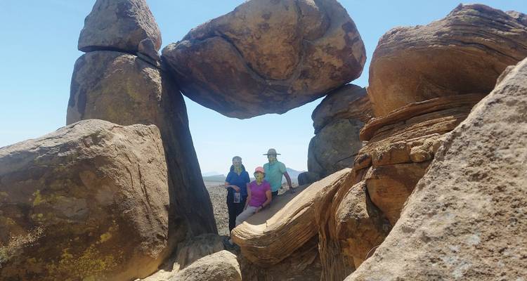 Drei Personen posieren unter großen Felsformationen.
