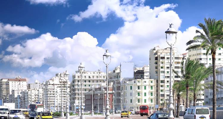 Concurrido bulevar frente al agua con bloques de apartamentos de mediados de siglo en blanco bajo nubes brillantes en Alejandría.