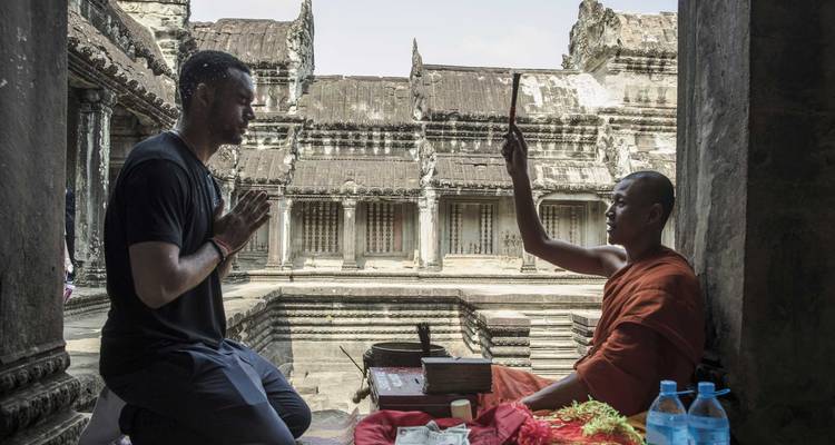 A monk performing a blessing ceremony inside a temple with a visitor kneeling.