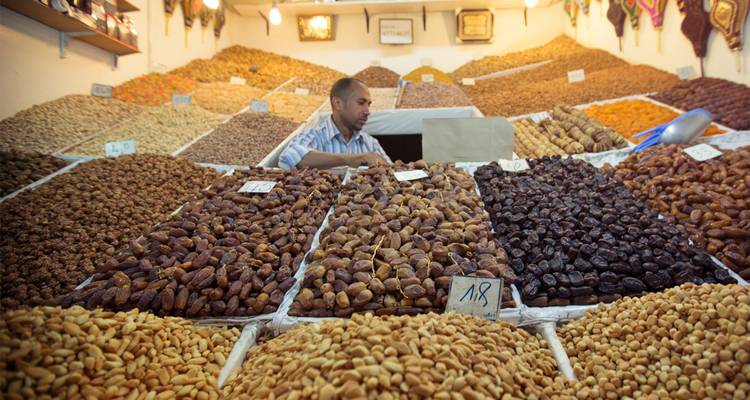 Comerciante acomodando pilas de dátiles, higos y nueces en un colorido puesto de mercado.