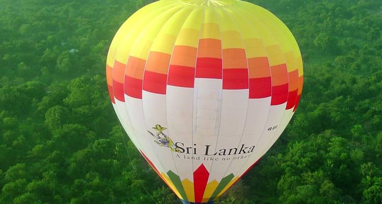 Brightly colored hot-air balloon emblazoned with 'Sri Lanka' drifts above emerald forest canopy.