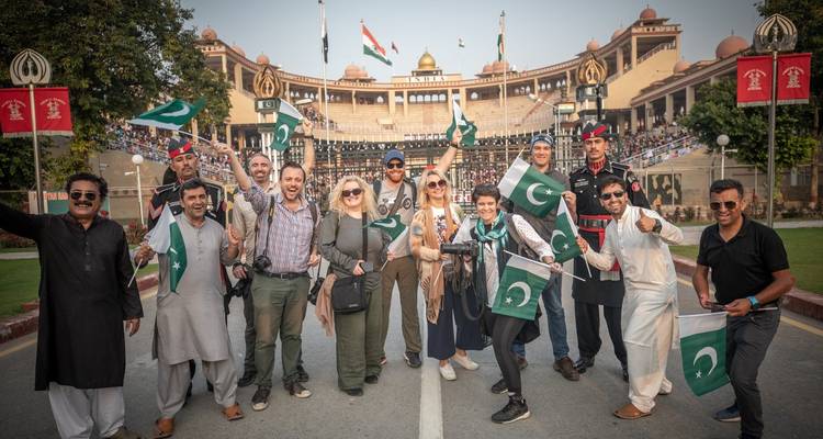 Große Gruppe, die bei einer zeremoniellen Grenzveranstaltung Fahnen schwenkt.