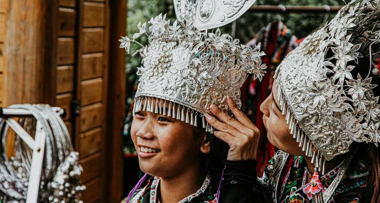 Mujeres jóvenes Miao probándose elaborados tocados de plata en un mercado cultural.