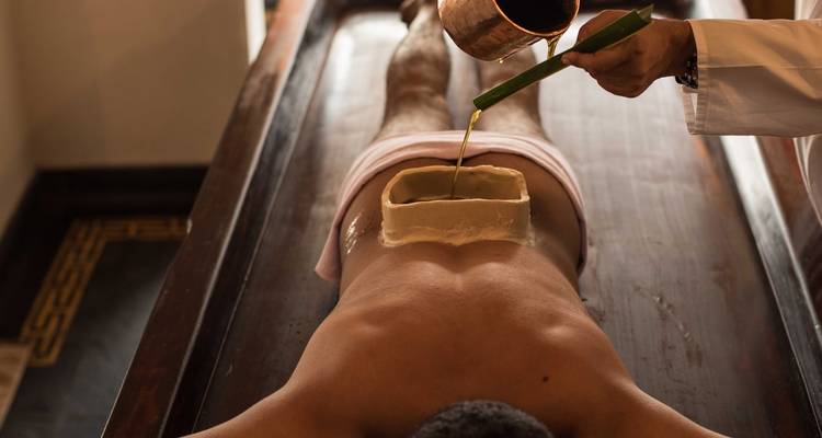 Een traditionele Ayurvedische oliebehandeling die wordt uitgevoerd op een persoon die op zijn buik ligt.