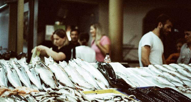 Binnenshot van meerdere mensen op een vismarkt met uitgestalde vis.