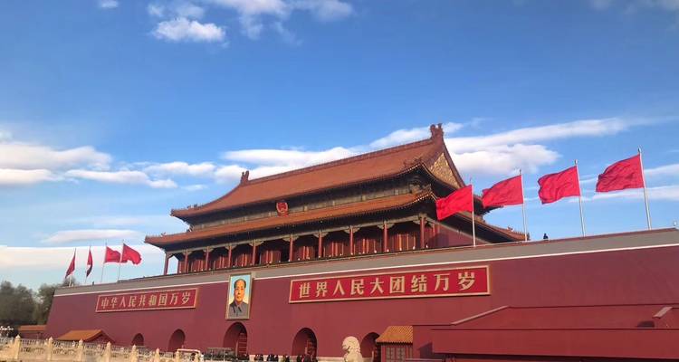 La Puerta de Tiananmen adornada con banderas rojas bajo un cielo azul domina la plaza histórica de Pekín.