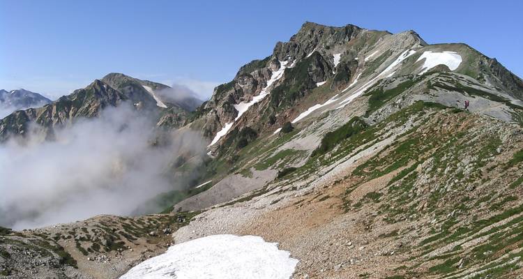 Cresta alpina rocosa con parches de nieve persistente y nubes a la deriva bajo los picos