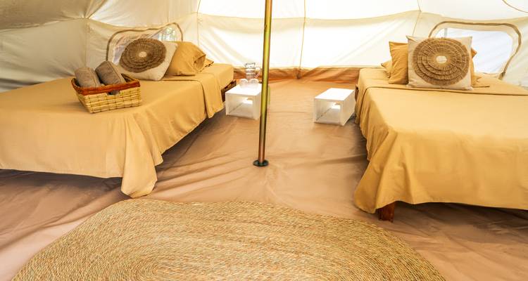 Interior de una tienda de campaña con dos camas y mobiliario sencillo.
