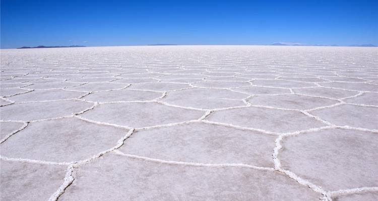 Endloses sechseckiges Muster des strahlend weißen Salar de Uyuni unter wolkenlosem blauen Himmel.