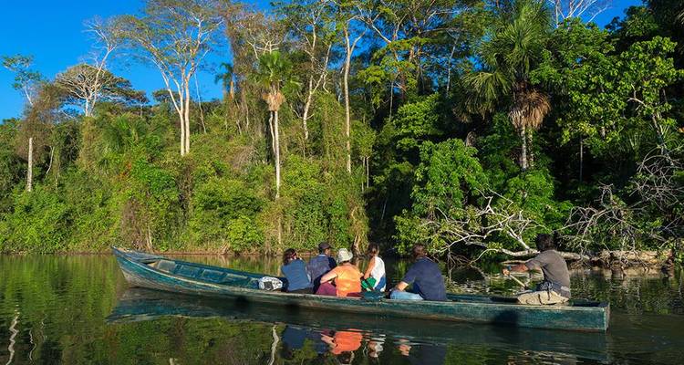 Voyageurs assis dans une longue barque en bois glissant sur les eaux calmes de la jungle avec une rive verdoyante