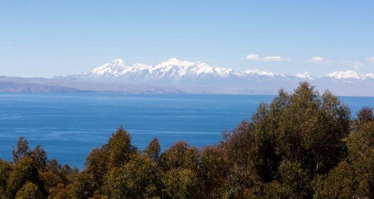 Les Andes enneigées se dressent au-delà de l'immense étendue bleu profond du lac Titicaca sous un ciel dégagé.