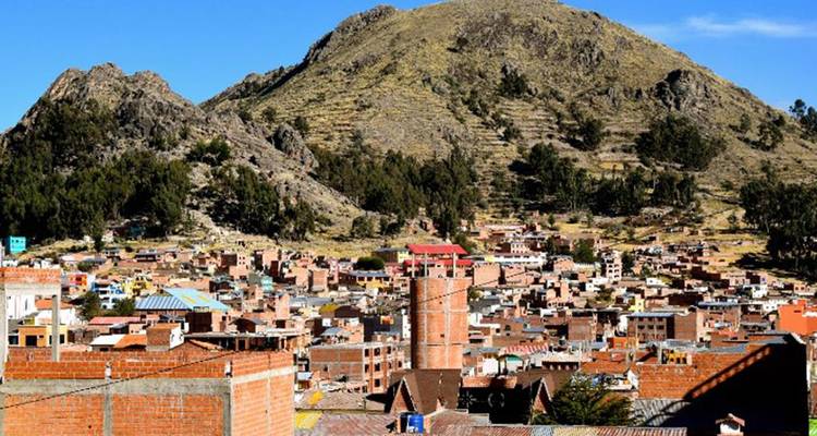 El pueblo de Copacabana con edificios de ladrillo anidados bajo el pico de una montaña verde y rocosa.