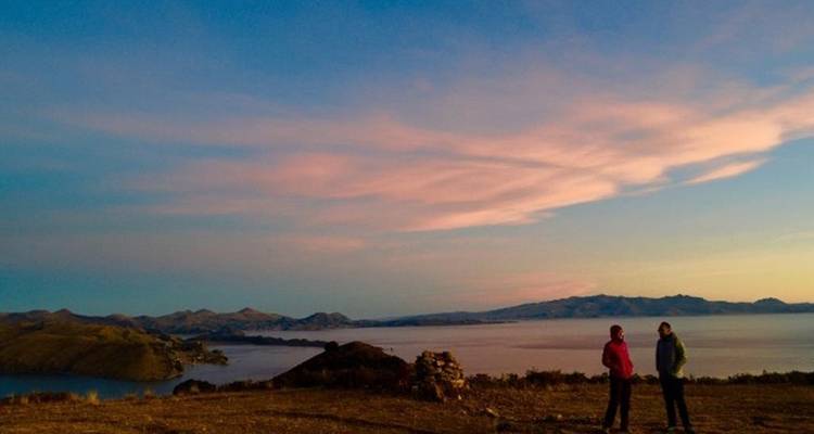 Deux voyageurs se tiennent sur une crête avec vue sur le Lac Titicaca au coucher de soleil coloré.