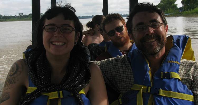 Smiling travellers wearing life jackets on a motorboat moving along a river.