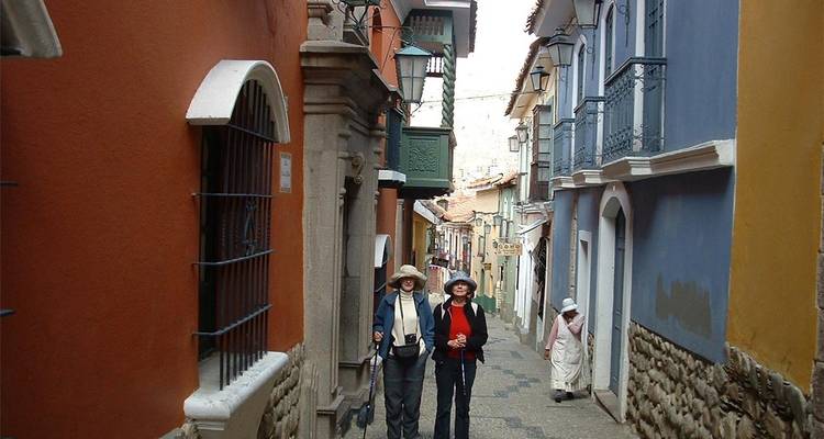 Travellers walking through a narrow colourful colonial street with balcony railings and stone walls.
