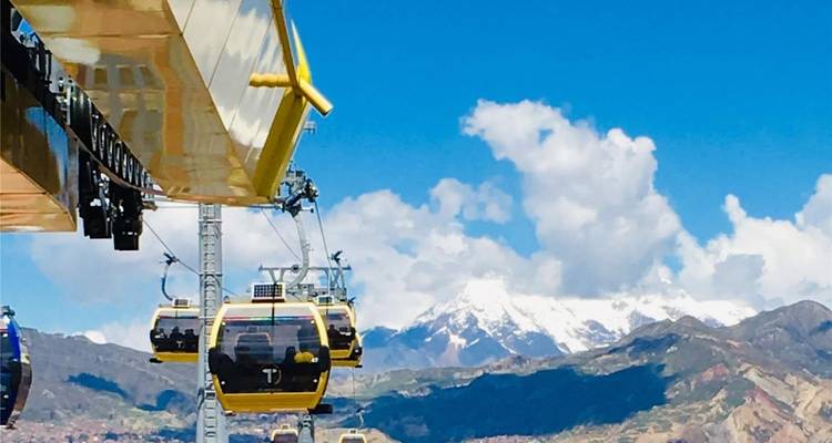 Bright yellow gondola cable cars gliding over La Paz with snowy Andean peak in the distance.