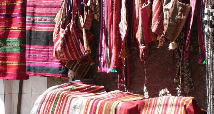 Vibrant Bolivian woven textiles and bags hanging in a sunlit market stall.