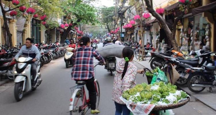 Rue animée de Hanoi bondée de motos, de cyclistes et de lanternes roses suspendues aux arbres.