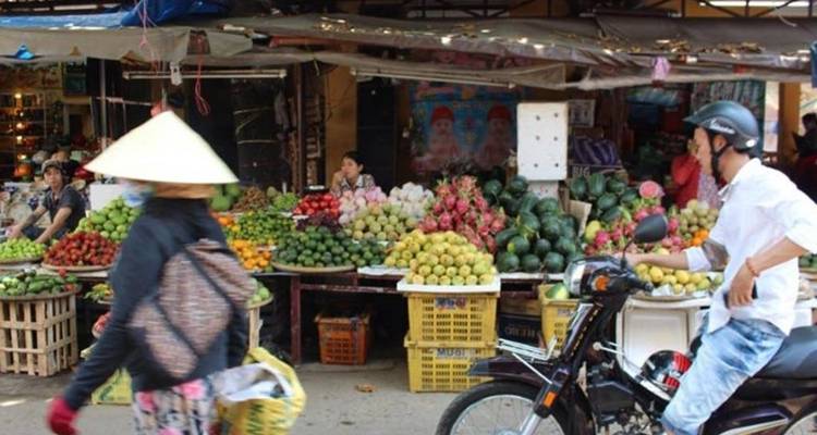 Marché aux fruits coloré à Hanoï avec des vendeurs, des paniers de produits et des motos qui passent.