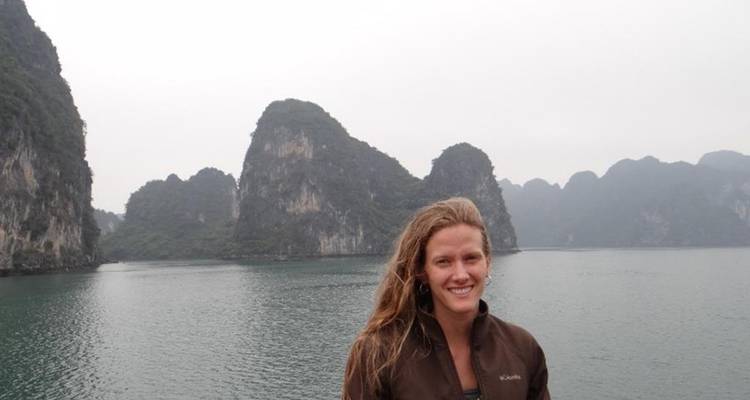 Un voyageur se tient devant des pics calcaires karstiques enveloppés de brume s'élevant des eaux tranquilles de la baie d'Halong.