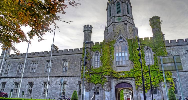 Steinernes Universitätsgebäude in Galway, das mit Efeu bewachsen ist und Celtic-Revival-Architektur unter sanftem Licht aufweist.