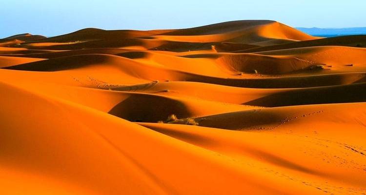 Vast and smooth sand dunes under a blue sky.