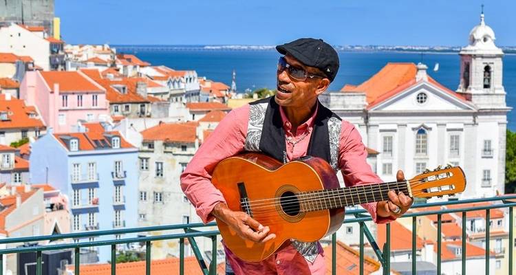 Homme jouant de la guitare avec en arrière-plan des bâtiments colorés de la ville et une vue sur l'eau.