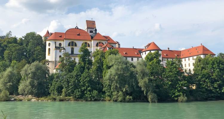 Grand bâtiment historique au bord d'une rivière avec un environnement verdoyant.