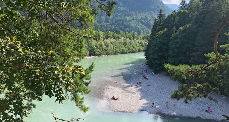 Une rivière entourée d'arbres verts luxuriants et des gens sur une zone de plage de galets.