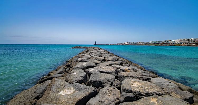 Jetée rocheuse s'étendant dans la mer turquoise avec un ciel dégagé.