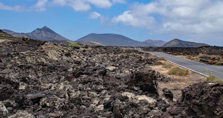 Un paysage aride avec des roches volcaniques et des montagnes lointaines sous un ciel bleu.
