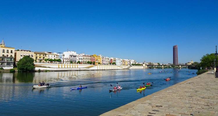 Kajakfahrer, die auf dem Guadalquivir-Fluss paddeln, mit bunten Häusern am Flussufer und einem modernen Turm in der Ferne