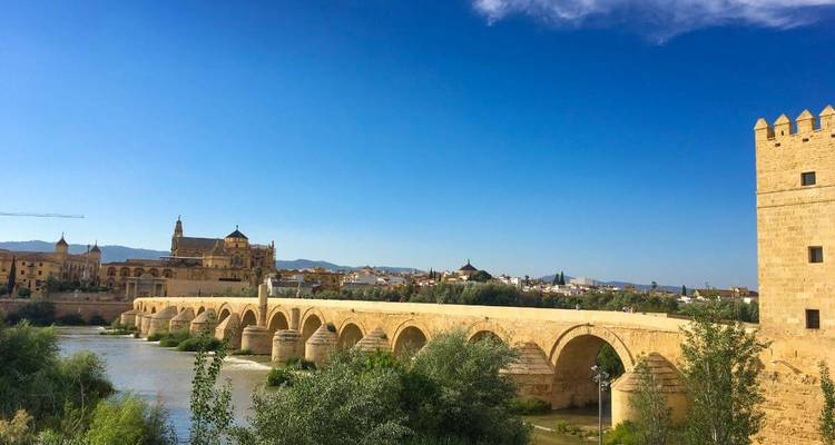 Historische römische Brücke, die den Guadalquivir überquert, mit der Moschee-Kathedrale von Cordoba im Hintergrund unter klarem Himmel