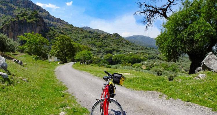 Rotes Tourenfahrrad auf einem Kiesweg geparkt, der sich durch ein bergiges grünes Tal schlängelt